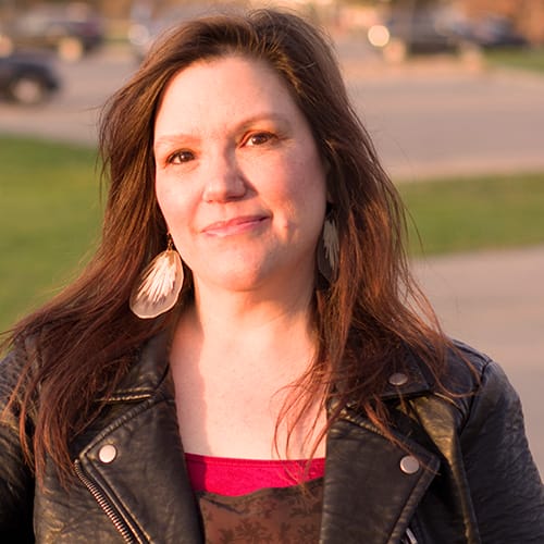 Charlotte Easterling smiles and faces the camera. She wears porcupine quill earrings, a red and black shirt, and a black leather jacket.