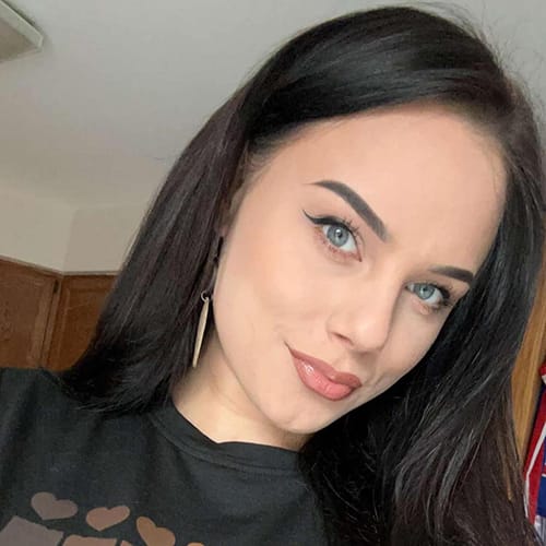 Misha Golly smiles and faces the camera. She wears a black t-shirt and earrings.